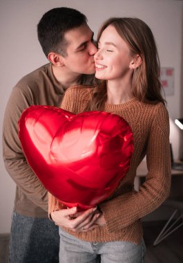 Sevgililer günün kutlu olsun. Genç bir çift ellerinde kalp şeklinde bir balon tutarak evdeki oturma odasında birbirlerine sevgiyle bakıyorlar. Evde tarih