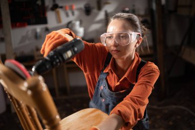 Atölyedeki Kadın Sanatçı elektrikli tornavidayla Tahta Sandalyeyi monte et. İş yerinde çalışan kadın marangoz. Boşluğu kopyala