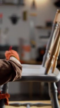 Serbest çalışan kadın marangoz, marangozluk atölyesinde tahta sandalyeyi gri boyayla boyuyor. Dikey video