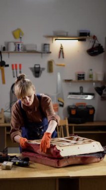 Yaşlı kadın mobilya restoratörü eski koltuğun parçalarını söküp atölyede döşeme yenilemeye hazırlıyor.