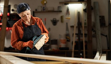 Dişi marangoz, atölyede dikilirken zımpara makinesini cilalamak için tutuyor. Boşluğu kopyala