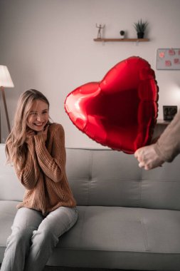 Sevgililer Günün kutlu olsun. Genç adam, oturma odasındaki kanepede oturan kız arkadaşına kalp şeklinde balon hediye ediyor. Romantik randevu
