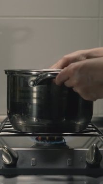 Kadın ev hanımı yemek pişiriyor, çelik tencereyi gaz ocağına koyuyor. Yakın plan. Dikey video