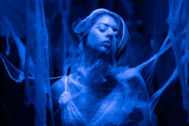 Mavi ışıkla aydınlatılan, duygusal yoğunluğu ve dramatik görsel etkiyi vurgulayan, ezici düşünceleri sembolize eden ağlara sarılı bir kadının gerçeküstü sahnesi..