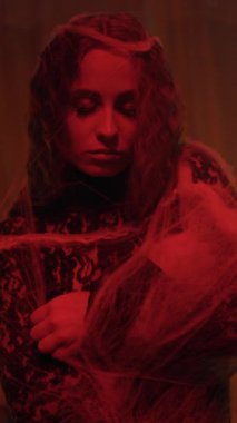 Siyah dantelli örümcek ağıyla makyajlı güzel Gotik kız. Kırmızı ışıkta uzun saçlı siyah prenses. Örümcek kadın ağ örüyor. Dikey video