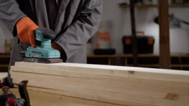 Marangoz, marangoz dükkanında elektrikli zımpara makinesiyle çalışan turuncu eldivenler giyiyor. Boşluğu kopyala