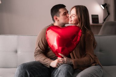 Kanepede aşık güzel bir çift kırmızı kalp şeklinde balon tutarken sevgililer gününü sevgilisiyle kutlayan genç bir adam ya da sıcak oturma odasında randevusu olan bir kadın..