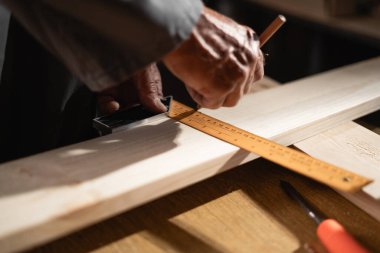 Marangozun atölyesindeki ahşap bir kalasın ölçümünü aldığı yakın plan. Boşluğu kopyala
