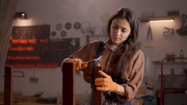 Bir restorasyon projesi sırasında koltuğun sıkışmış bir parçasını çıkarmak için çekiç kullanan bir kadın. Göreve dikkatle odaklanılıyor.