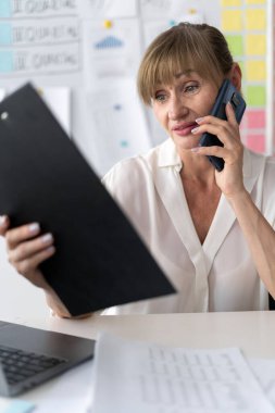 Ofiste telefon ve iletişim. Cep telefonuyla konuşan ve iş yerinde pano tutan bir kadın ya da çalışan. Boşluğu kopyala