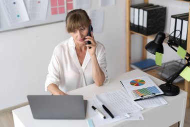 Ofiste cep telefonu ve dizüstü bilgisayarla çalışan ve iyi bir işi olan olgun çekici bir iş kadını. Boşluğu kopyala