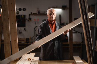 Kıdemli adam atölyesinde büyük bir tahta tutuyor. Küçük işletmelerdeki yaşlı işçilerin beceri ve adanmışlıklarını sergilemek, işçiliği ve deneyimi ön plana çıkarmak.