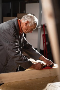 Yaşlı bir zanaatkar ahşap bir tahta uçurur, talaş ve toz yaratır, marangozluk atölyesinde. Boşluğu kopyala