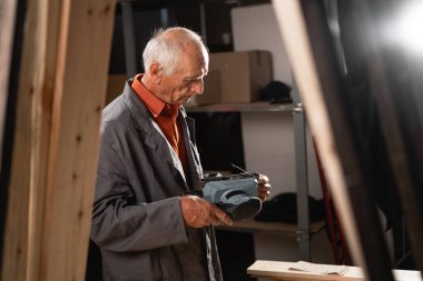 Marangoz atölyesinde elektrikli zımpara makinesi kullanarak ahşap kalas zımparalıyor. Zımpara makinesinin zımpara kağıdını değiştiriyor, ahşap işçiliği becerileri ve adanmışlığı gösteriyor..