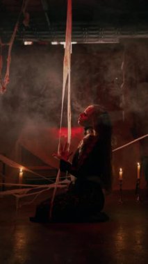 Büyüleyici bir cadı antik bir şatonun zemininde oturuyor, ilgisiz bir şekilde örümcek ağlarına dokunuyor. Karanlık, mistik atmosfer onun gizemli, vampirvari varlığını vurguluyor. Cadılar Bayramı. Boşluğu kopyala.