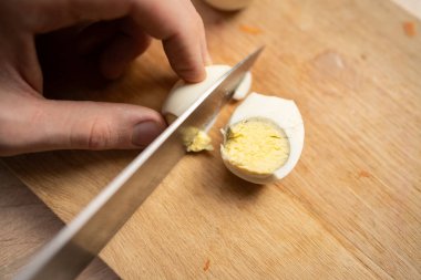 Haşlanmış yumurtayı tahtadan ikiye bölen adam kahvaltıyı evde hazırlıyor, kapat.