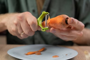 Bir insanın ellerinin, olgun havucu temizlemek için sebze soyacağı kullanması, ev yemeği ve yemek hazırlama kavramını hassasiyetle ve özenle gözler önüne seriyor..