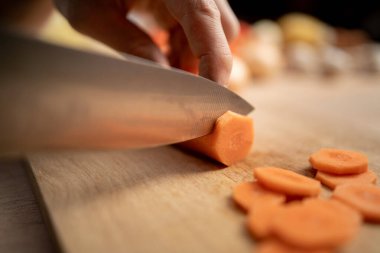Tahta bir masada büyük bir bıçakla taze havuç keser ve yemeye hazırlanır. Yakın plan.
