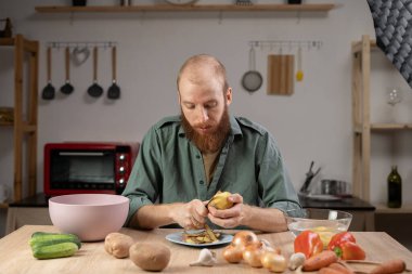 Mutfakta havuç soyan ve sebze soyan bir adam. Boşluğu kopyala