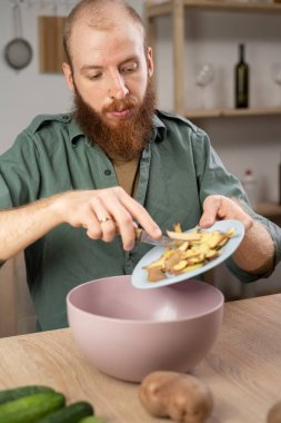 Sakallı beyaz adam geri dönüşüm için patates kabuklarını atıyor. Evde organik atık gübrelemek. Evde erkek aşçı yemek artıklarını plastik kaseye koyar. Boşluğu kopyala