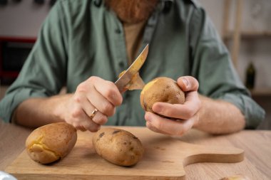 Adam patatesleri bıçakla ve elleriyle temizliyor. yakın plan