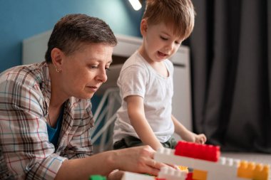 Orta yaşlı bir anne, evde yerde yatarken 4 yaşındaki oğluna plastik bir ev inşa etmede yardım ediyor. Birlikte kaliteli vakit geçirmeyi, oyun oynamayı ve eğlenmeyi seviyorlar.