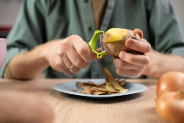 Adam mutfağında yemek pişirirken taze patatesleri tabağın altında soyuyor.