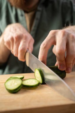 Salata için taze salatalık kesen mutfak bıçağıyla erkek eli. Boşluğu kopyala