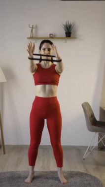 Oturma odasında elleri için direniş bandıyla egzersiz yapan genç bir kadın. Dikey video