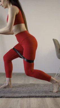 İspanyol kadın direniş bandı çömelmesi yapıyor spor kıyafetleri giyiyor, evde rutin oturma odası egzersizi yapıyor. Dikey video