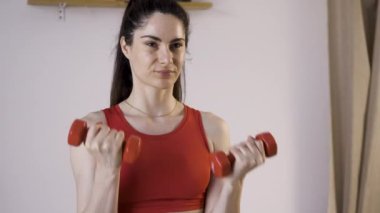 İspanyol kadın, oturma odasında spor kıyafetleri içinde halterlerle egzersiz yapıyor. Spor ve spor konsepti