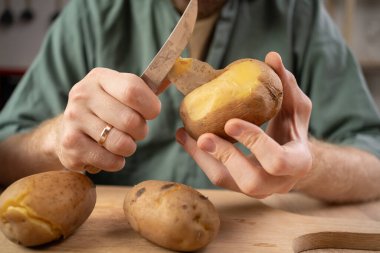 Patates salatası için mutfakta haşlanmış patatesleri soyan adamın yakın çekimi. Boşluğu kopyala