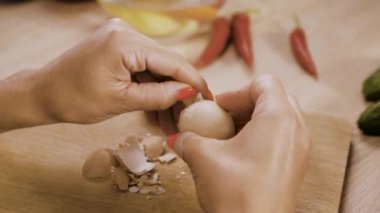Kadın ellerinin yakın çekimi haşlanmış yumurtayı soyar. Deniz kabuğundan yumurta soymak. Akşam yemeği ya da haşlanmış yumurtalı salata. Yakın çekim.