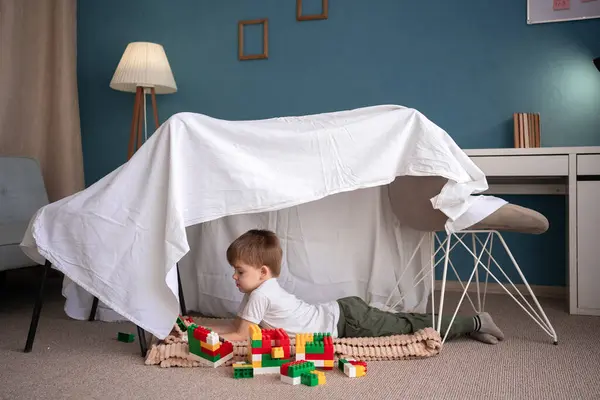 stock image Happy adorable child boy playing in play tent, in handmade toy fort from chairs and blanket. Copy space