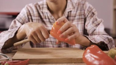 Tanımlanamayan bir kadın evdeki mutfağında bir masada otururken kırmızı bir dolma biberin çekirdeğini bıçakla kesip oyuyor. Yakın plan.