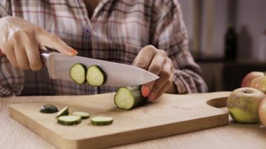 Kesme tahtasındaki salatalıkları dilimlemek. Kadın aşçı ev mutfağında sebze salatası pişiriyor. Yakın plan.