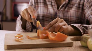 Mutfakta ahşap kesme tahtasıyla tatlı kırmızı biberi dilimleyen kadının yakın çekimi. Boşluğu kopyala