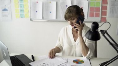 Ofisteki masasında çalışan kıdemli bayan yönetici cep telefonunu alıyor ve muhasebe raporlarını okuyor. Boşluğu kopyala