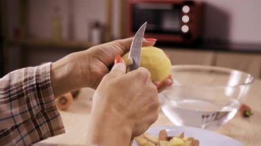 Bir kadın evde yemek hazırlar, patates soyar ve suya koyar. Yakın plan.