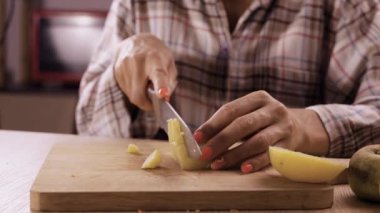 Mutfağında tahtanın üzerinde bıçakla haşlanmış patatesleri kesen bir kadın. Yakın plan.