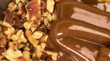 Kalın bir karamel akıntısı ahşap bir kesme tahtasına ceviz dökerek zengin ve lezzetli bir tatlı malzemesi yaratıyor. Tatlı karamel ve cevizlerin karışımı.