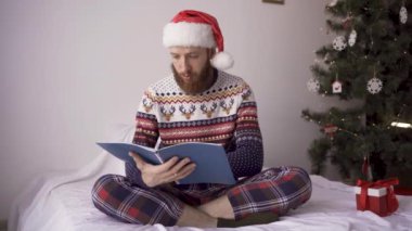 Noel Baba şapkalı ve kazaklı sakallı adam yatağında oturmuş günlüğünü okuyor. Boşluğu kopyala