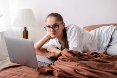 Genç bir kadın evde dizüstü bilgisayardan ilginç bir film izlerken kahverengi bir yatakta uzanıyor. Boşluğu kopyala