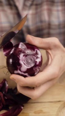 Adam ev mutfağında kırmızı soğan soyuyor. Erkek eli salata soğanı tutuyor. Dikey video