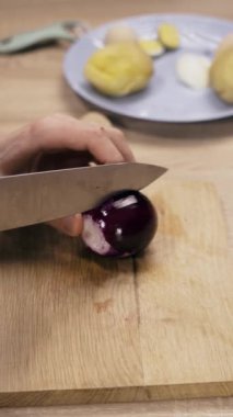Erkek ellerinin ahşap tahtada olgun kırmızı soğan kestiği yakın plan, üst manzara. Dikey video