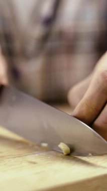 Şefin elleri, sarımsağı tahta bir kesme tahtasının üzerinde doğruyor. Yemek sosu. Yakın plan.