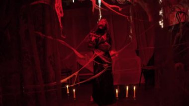 Örümcek ağı takan sanat fantezi kadın cadı karanlık gotik odada mum dolu sihirli eller yaratıyor. Siyah ve kırmızı