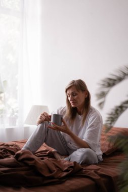 Sabah, eğlence ve insan konsepti. Yatak odasında yatağında bir fincan kahveyle yaşlı çekici bir kadın. Boşluğu kopyala