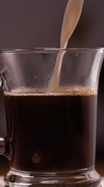 Şeffaf bardakta sade kahveye süt dökülüyor. Dikey video