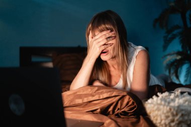 Orta yaşlı bir kadın geceleri yataktaki filme dramatik bir tepki vererek elleriyle yüzünü kapatıyor. Boşluğu kopyala